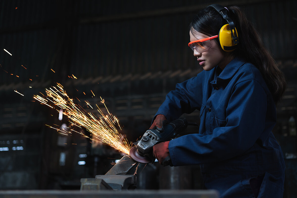 A female Asian engineer using angle grinder in factory workshop