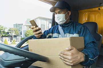 A delivery man holds parcel box while using smartphone in a van.