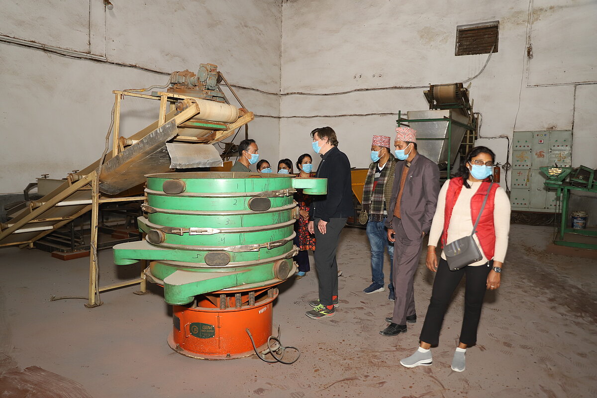 A group of around 8 people with face mask examining equipment in a factory.