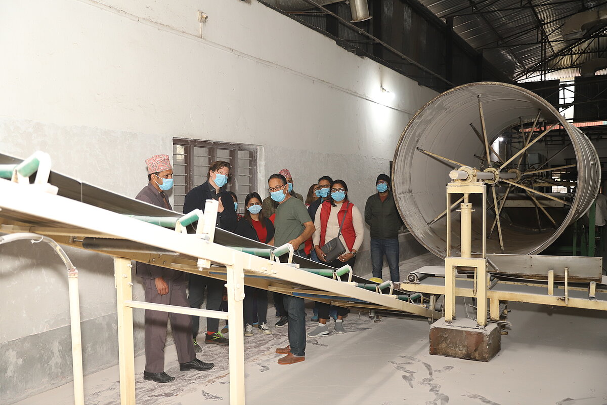 A group of around 10 people with face mask examining equipment in a factory.