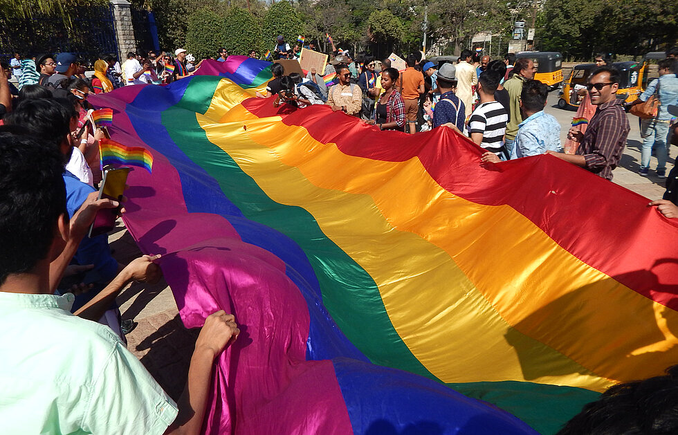 LGBT activists hold a long rainbow colored flag demanding equality.