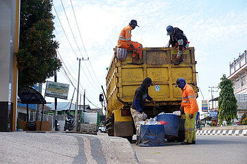 Workers dumps a trash can into a garbage truck at road side.