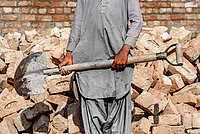 A photo of a man holding a shovel with a pile of bricks in the background