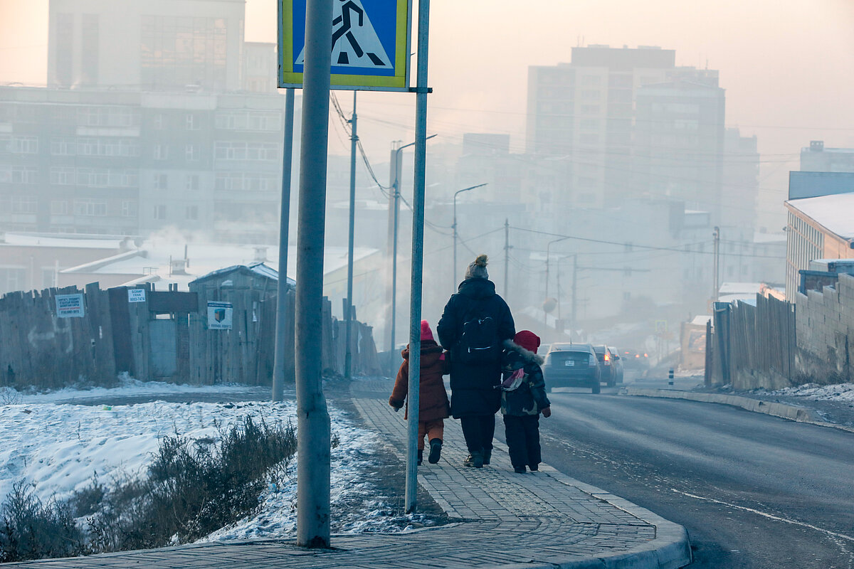 An adult with two children walking along a road covering with air pollution on a snowy day