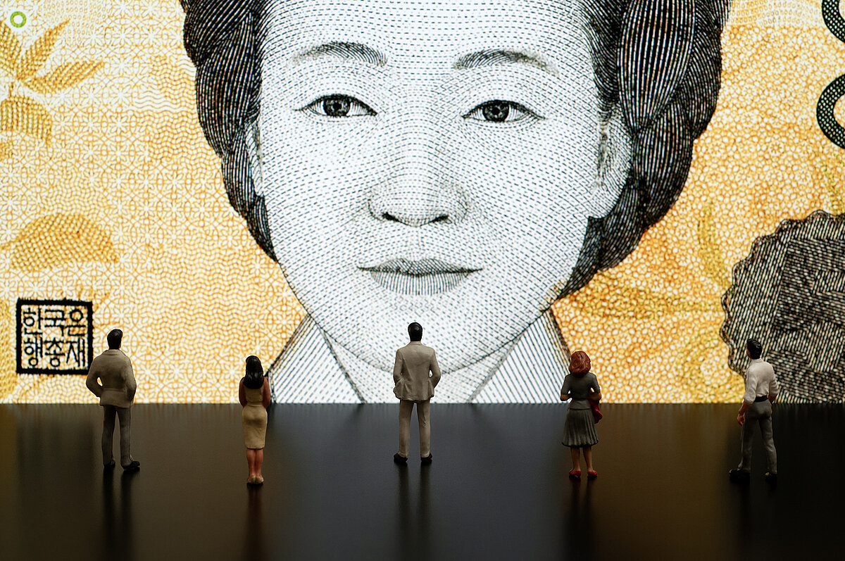 A huge image of Korean bank note and 4 small people standing in front of it looking at it.