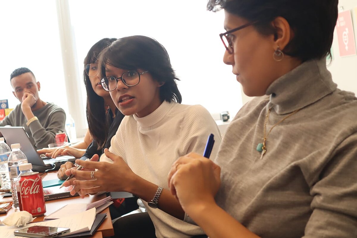 A photo of 4 participants, one male and 3 female sitting and talking, facing someone who is probably in front of the desk.