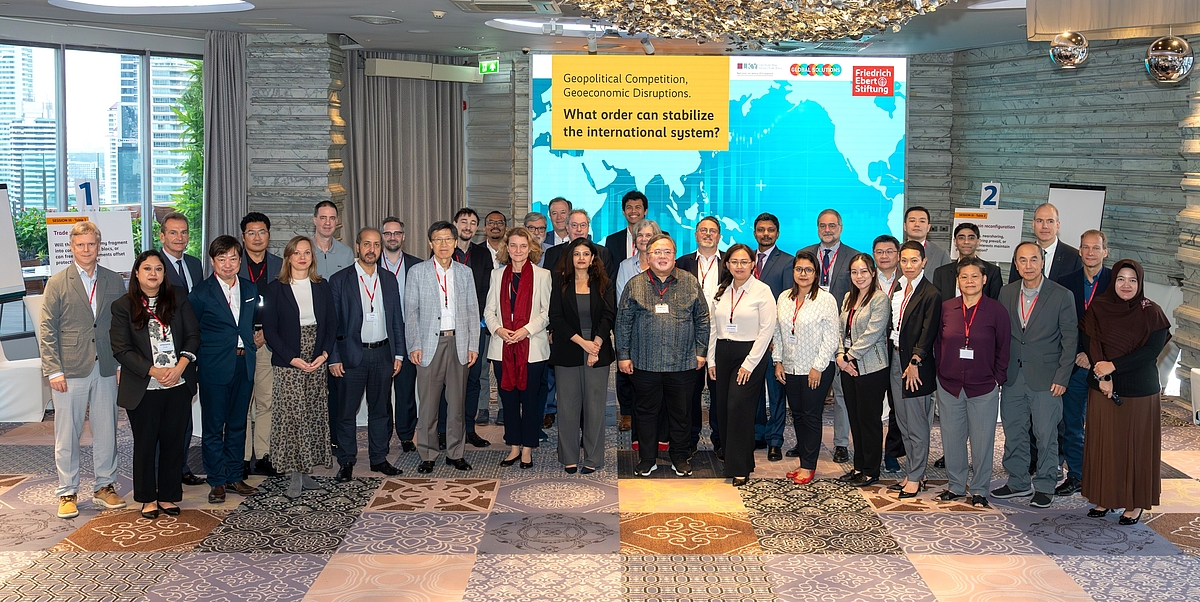 A group photo of around 30 people in an event hall with a screen at the background. The screen shows world map with event title: Geopolitical competition, Geoeconomic Disruptions. What order can stabilize the international system?
