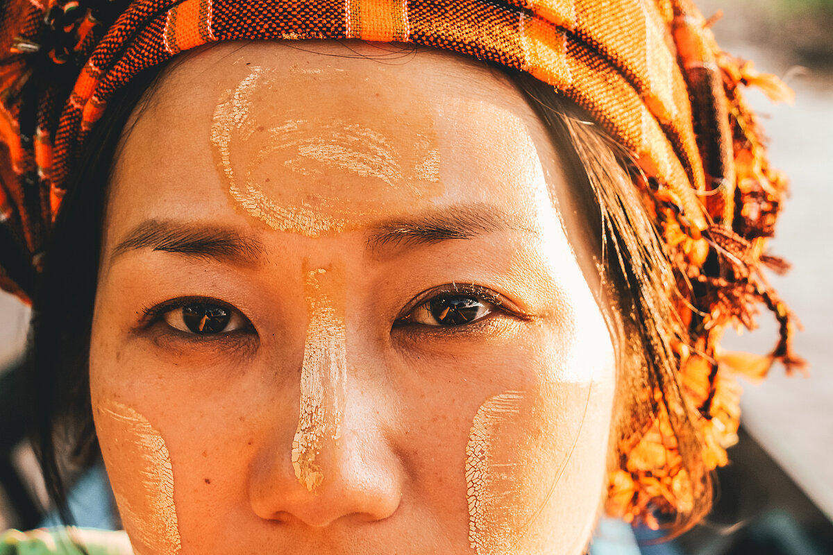 A woman in Myanmar with Thanaka powder on her face looking at camera