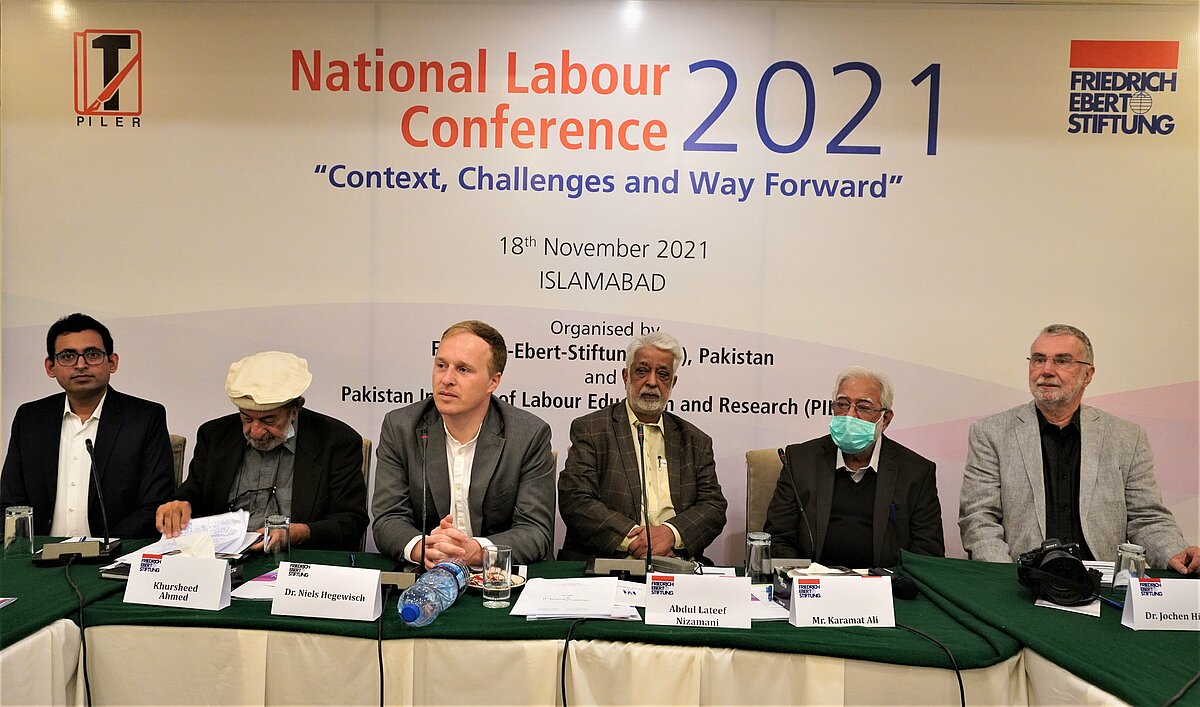 6 men sitting next to each other at a table druing the National labour Conference 2021 in Pakistan. 
