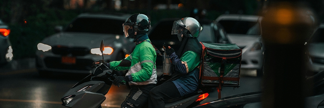Delivery driver in green uniform riding a motorbike on a street