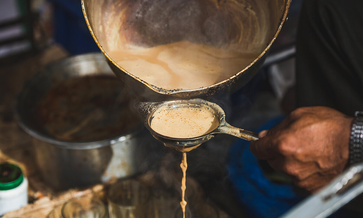 Hot masala milk tea is being poured from the pot to tea filter