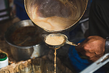 Hot masala milk tea is being poured from the pot to tea filter