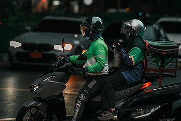 Delivery driver in green uniform riding a motorbike on a street