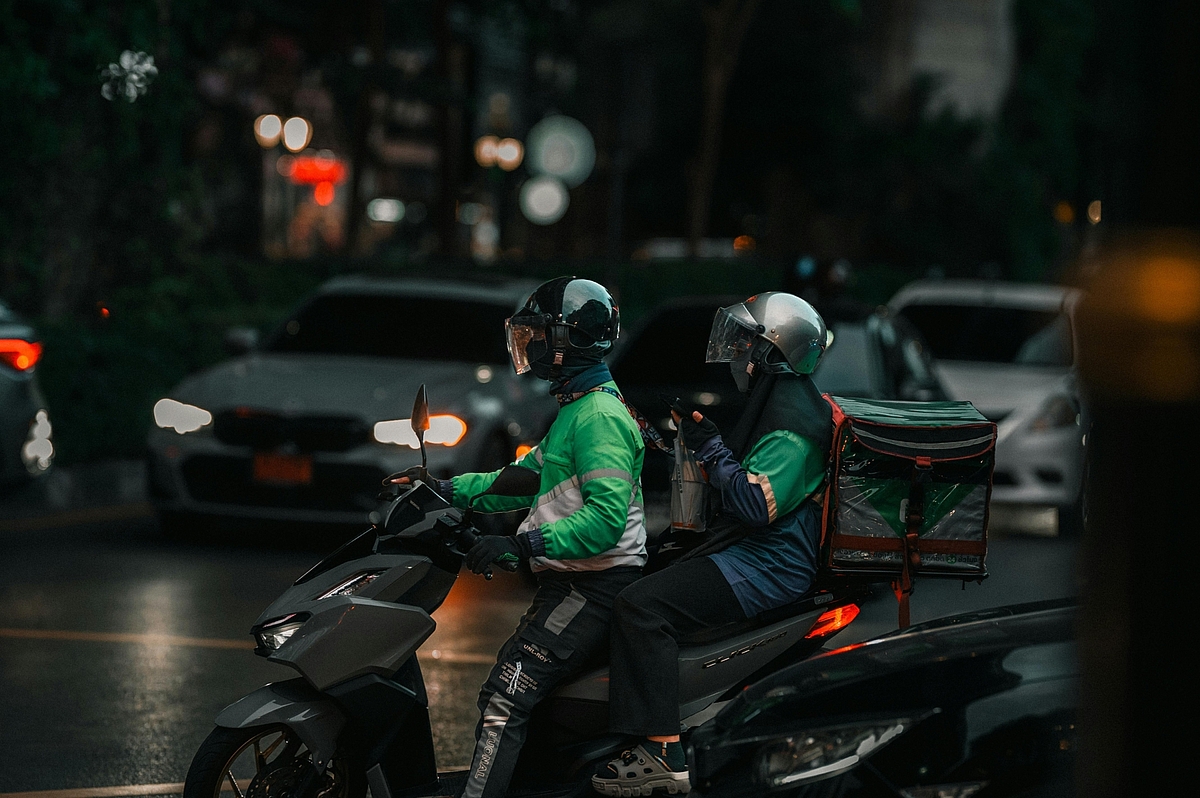 Delivery driver in green uniform riding a motorbike on a street