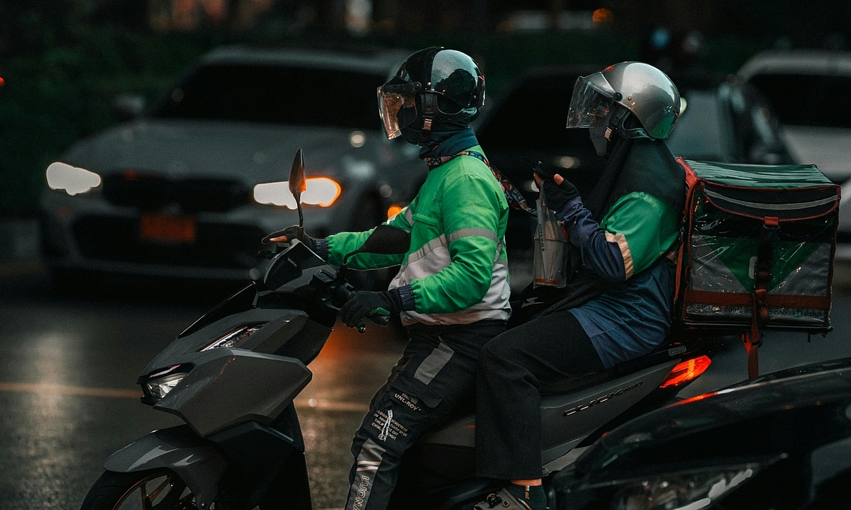 Delivery driver in green uniform riding a motorbike on a street