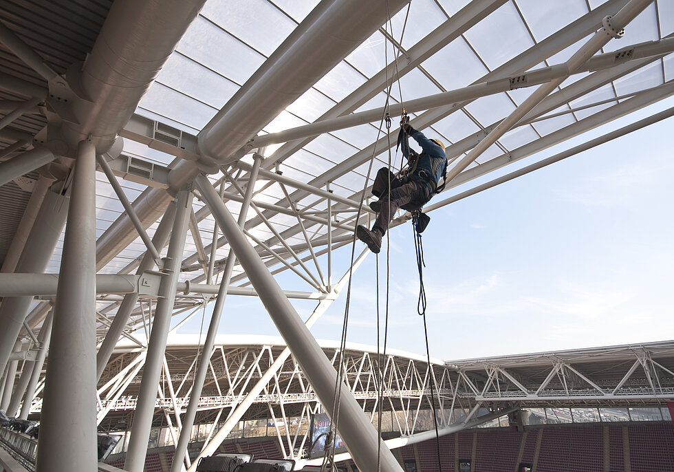 A worker climbing up the construction of stadium roof