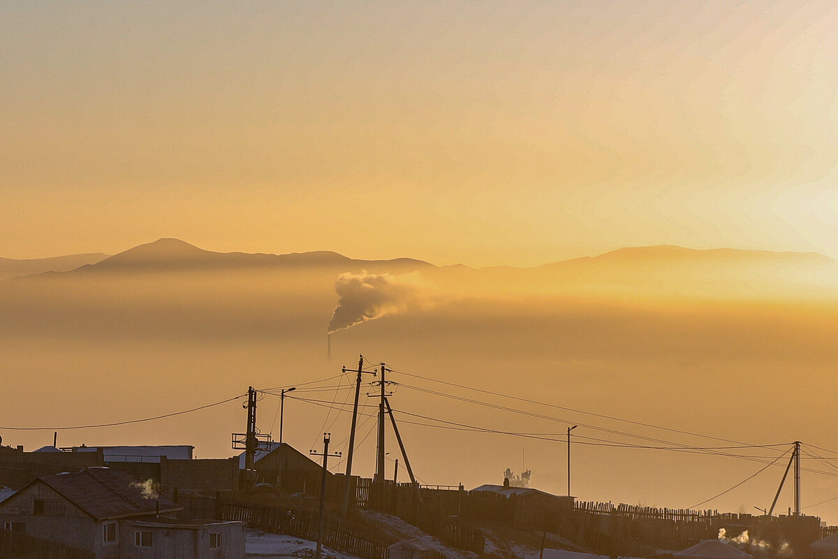 The yellow cloudy sky above the village with a chimney releasing smoke in the middle